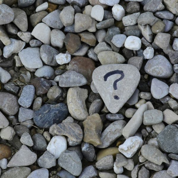 A stone with a question mark painted on it, surrounded by many pebbles