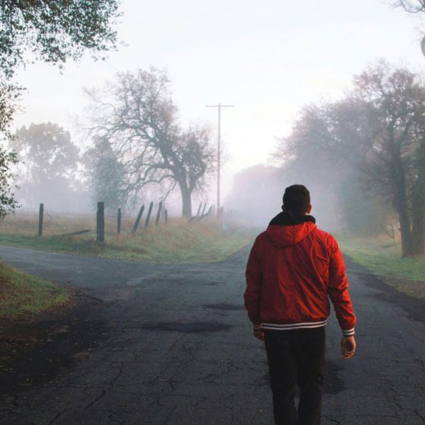 A man in a red jacket walks down a foggy road