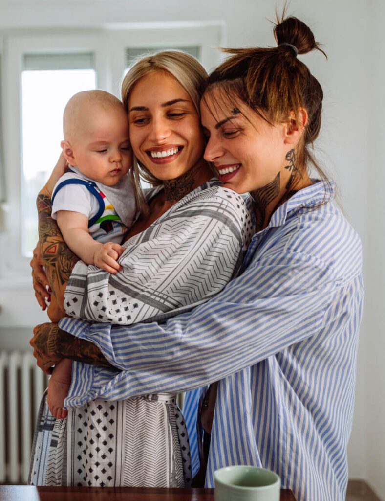 Two women with a tattoos on their arms hold a baby
