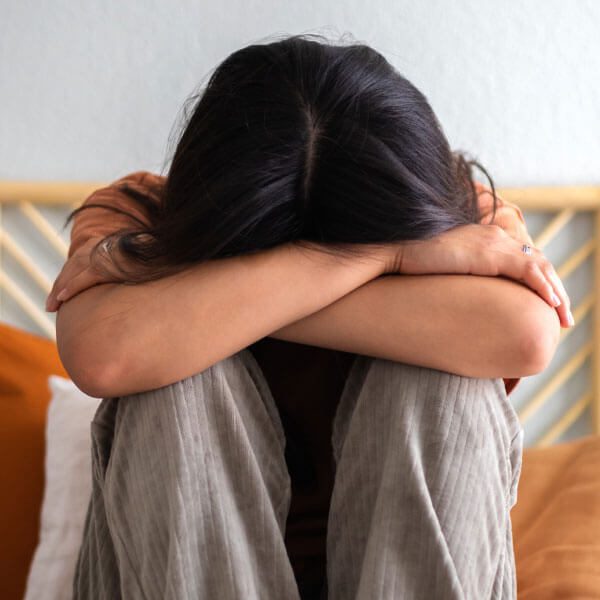 A woman sits on a bed with her head in her hands