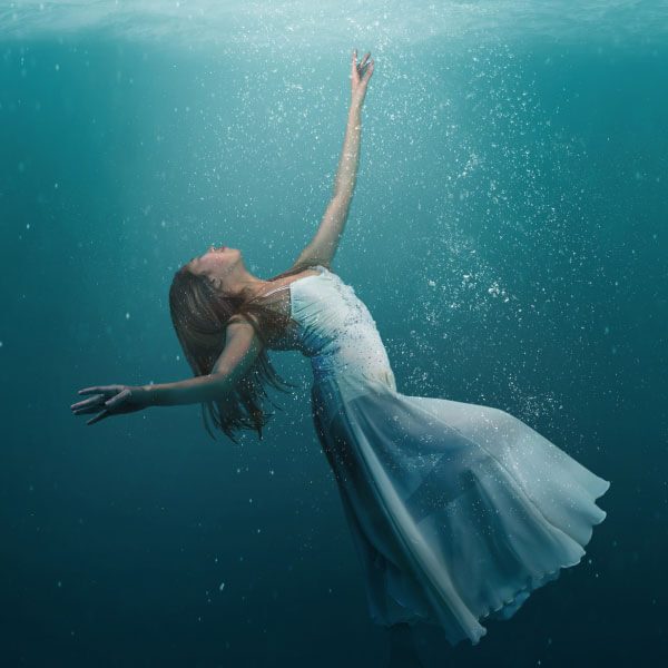 A woman in a white dress is floating underwater